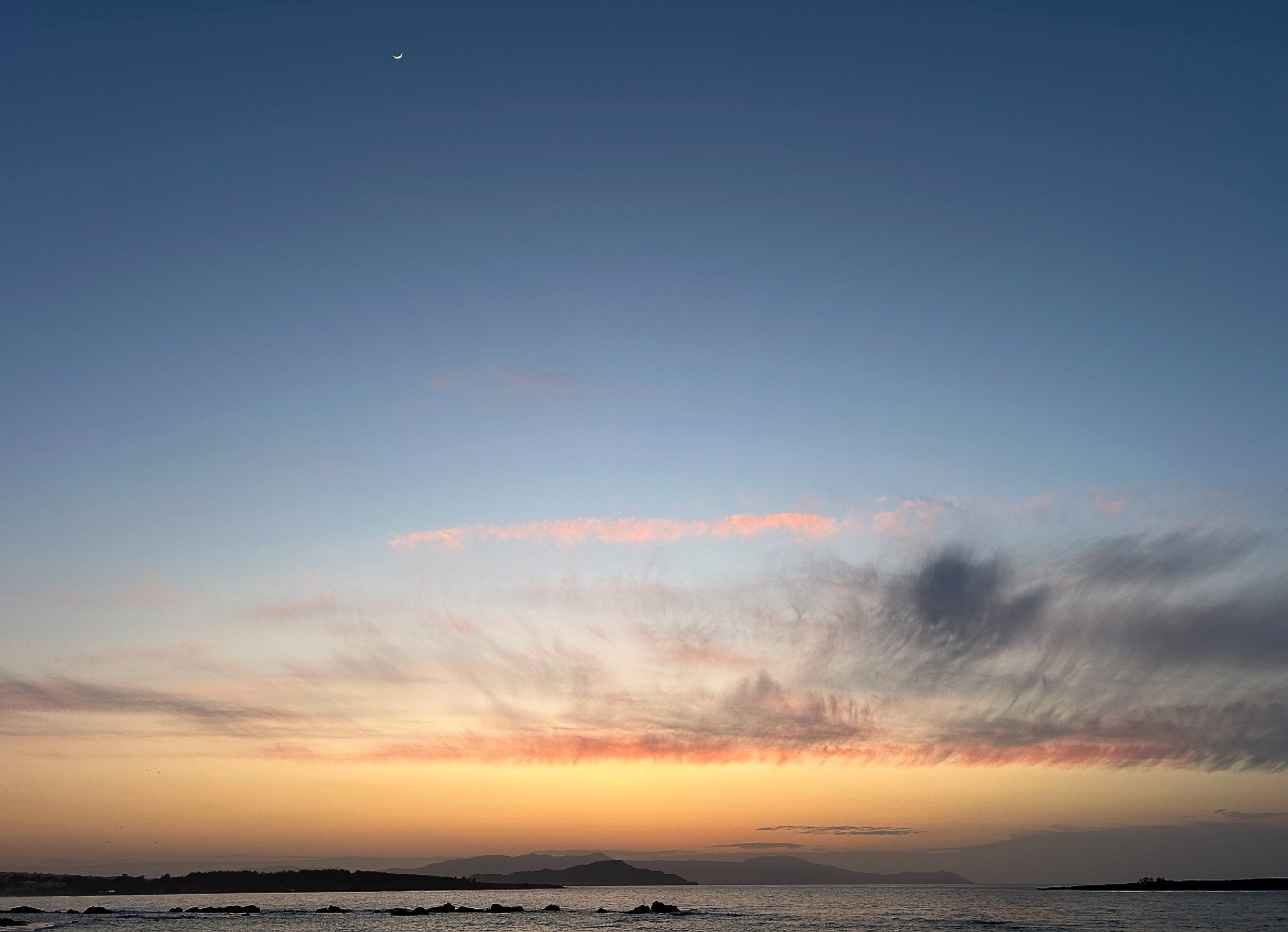 Sunset over the sea beneath a crescent moon