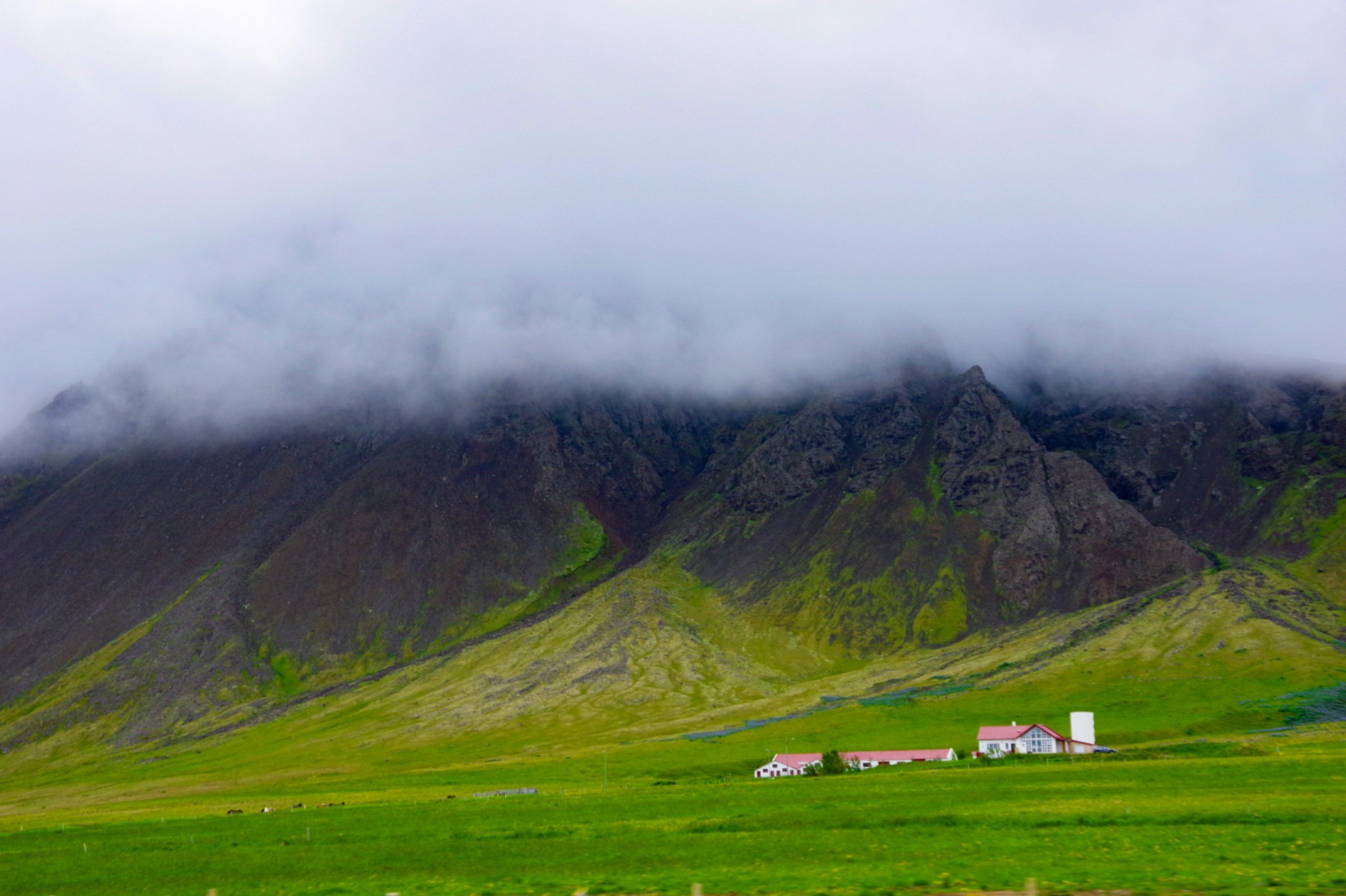 Fog rolling over an Icelandic mountain above a green farm